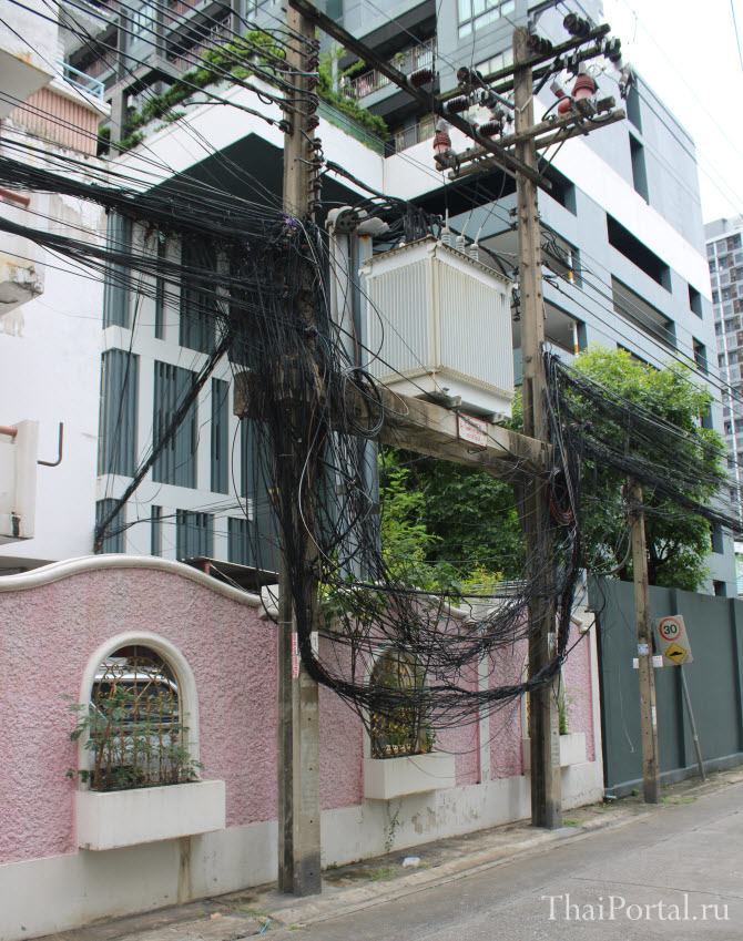 на фото мешанина из телекоммуникационных проводов, свисающая со столба над улицей в Бангкоке
